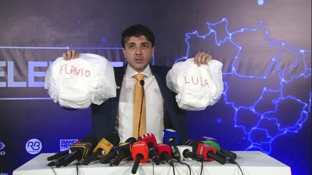 Renan Santos chega a debate presidencial com fraldas de Lula e Flávio em provocação; entenda